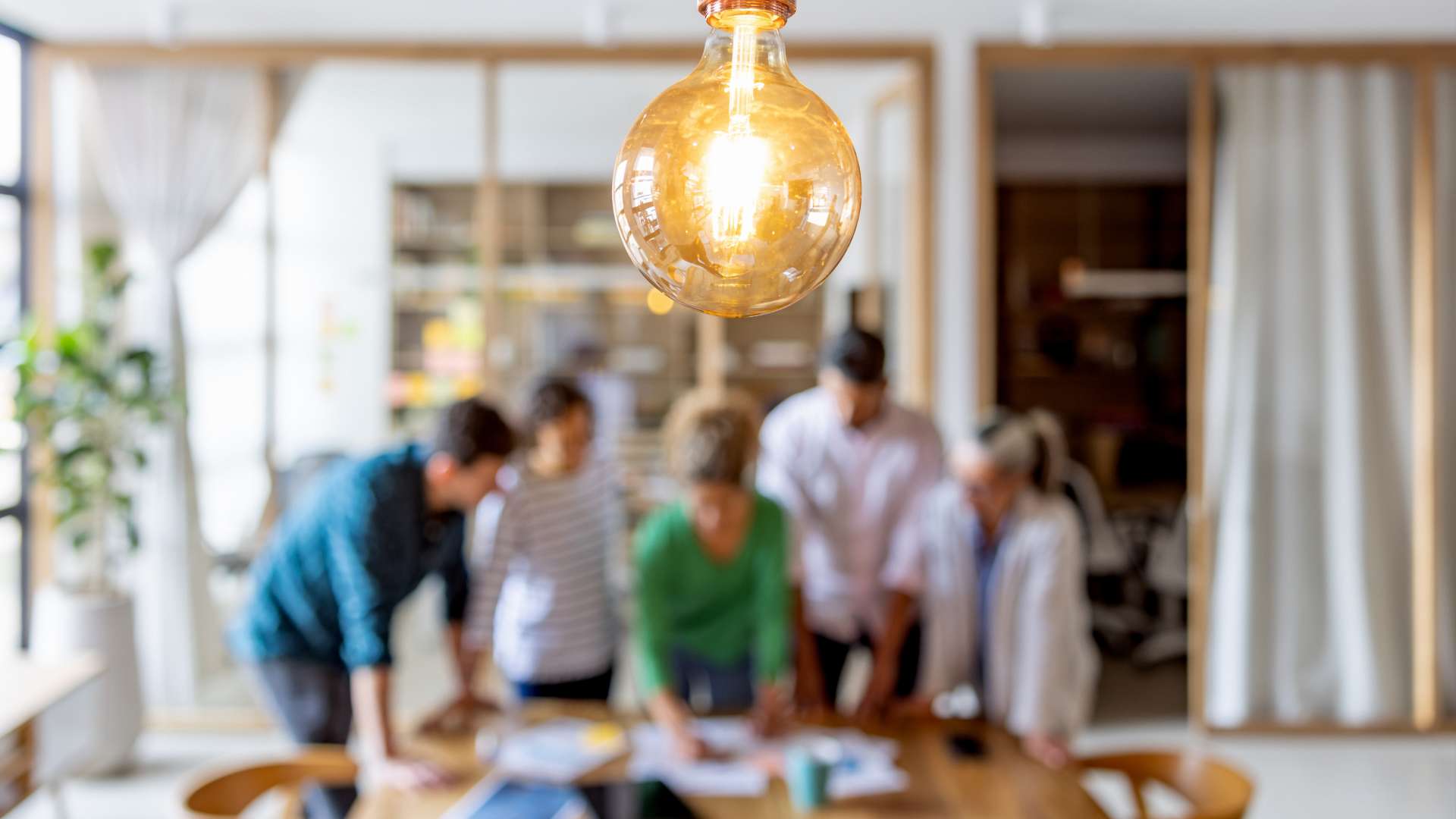 Technology – creative solutions A group gathered around a table looking at papers with a lighbulb in the foreground